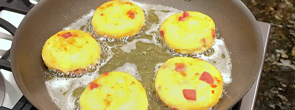 Tortitas de papa con salchicha dorándose en aceite